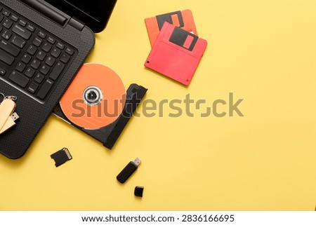 Laptop with CD disk and different memory storage devices on yellow background