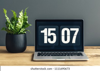Laptop With Clock Screensaver Placed On A Wooden Desk With Potted Plant