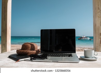 A Laptop Cofee Cup And Straw Hat On Wooden Table And Ocean View