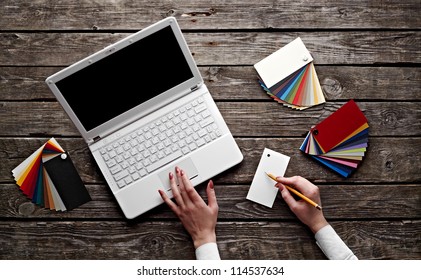 Laptop with color swatches with woman's hands holding pencil on old wooden table. Workplace designer. - Powered by Shutterstock