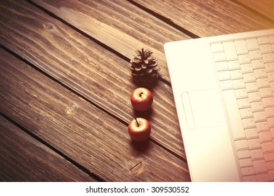 laptop computer and apples with pine cones on wooden background.