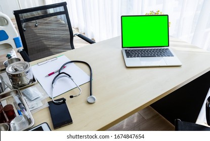 Laptop Computer With A Blank Green Screen With Stethoscope,vial,syringe,empty Paper Clipboard And Medical Bottle Different Drugs On Surgical Tray With Medical Equipment On Wooden Table Background