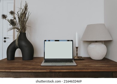 Laptop computer with blank screen on table with lamp and flowers bouquet. Aesthetic influencer boho styled home workspace interior design template with mockup copy space. Online store, blog branding