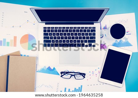 Laptop computer and documents report statistic financial with graph and chart and glasses and tablet, finance and invest, digital marketing and growth of revenue, business and communication concept.