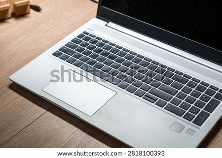 Laptop computer with full keyboard and numeric keypad on wooden desk surface, showing silver aluminum chassis and large trackpad, concept of remote work productivity