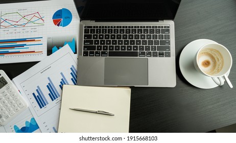 Laptop computer and graph with coffee cup on the black table in the office