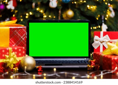 Laptop computer with green blank empty screen on table with gifts and garland