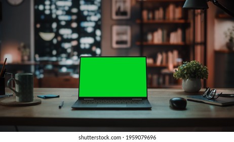 Laptop Computer with Mock Up Green Screen Display Standing on the Table in Cozy Living Room. In the Background Stylish Modern Home Office Studio in the Evening with Big Cityscape Window. - Powered by Shutterstock