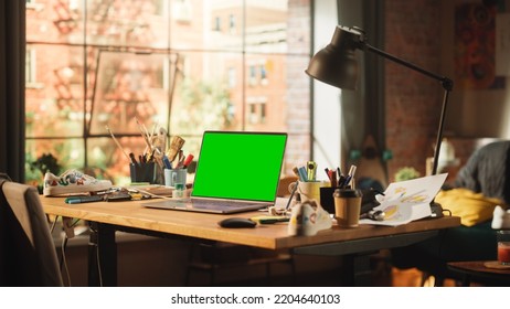 Laptop Computer With Mock Up Green Screen Chroma Key Display Standing On The Desk In The Modern Loft Workspace. Open Space Studio In The Background With City Window View.