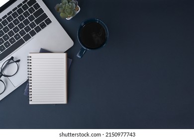 Laptop computer, notebook and coffee cup on dark blue background. Top view, copy space.