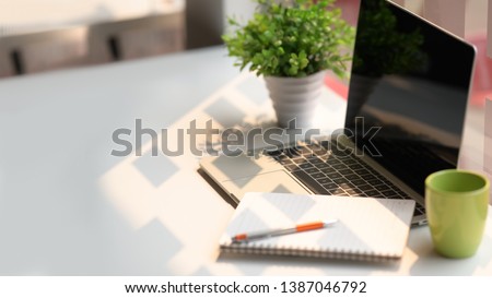Laptop computer with notebook, coffee on white table in office workspace.