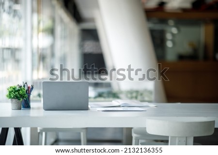 Laptop Computer, notebook, and eyeglasses sitting on a desk in a large open plan office space after working hours
