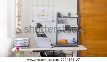 Laptop Computer, notebook, and eyeglasses sitting on a desk in a large open plan office space after working hours	