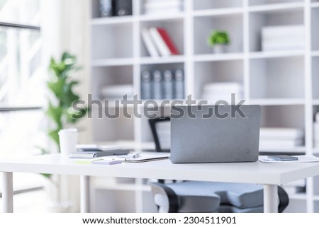 Laptop Computer, notebook, and eyeglasses sitting on a desk in a large open plan office space after working hours	
