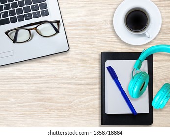 Laptop (computer), notebook, glasses, diary, blue pen, black coffee, Music headphones.
Put on a  light gray wooden table.
(with copy space)
