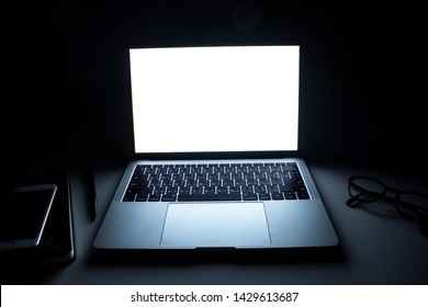 Laptop computer on the desk of a business worker in a dark room with light from one screen.