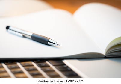 Laptop Computer On A Modern Wooden Business Desk With A Notepad And Pen In Unfocused Background.