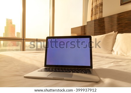 Laptop computer on white bed sheets in cozy hotel room with copy space blank screen