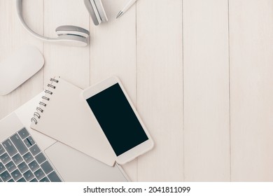 Laptop computer on white table with headphone and smartphone. View from above