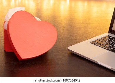 Laptop Computer And An Open Heart-shaped Gift Box On A Dark Wooden Table Against A Background Of Lights. Online Shopping And Chatting, Virtual Valentine's Day, Love In Time COVID-19 Concept.