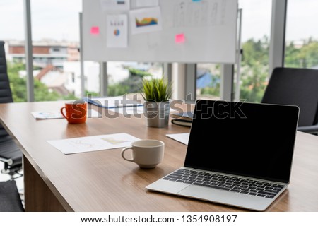 Laptop computer with opened lid on table in meeting room of office workspace.