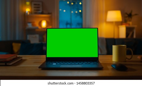 Laptop Computer Showing Green Key Screen Stands on a Desk in the Living Room. In the Background Cozy Living Room in the Evening with Warm Lights on. - Powered by Shutterstock