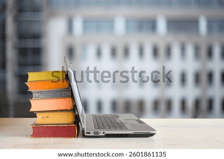 Laptop computer and stack of books ,blurred office building as background.Beat the clock,office work,education concept.Free copy space.