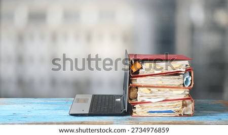 Laptop computer and stack of messy ringbinders with grungy business paperwork, bureaucracy,beat the clock,heavy workload concept. Blurred background.