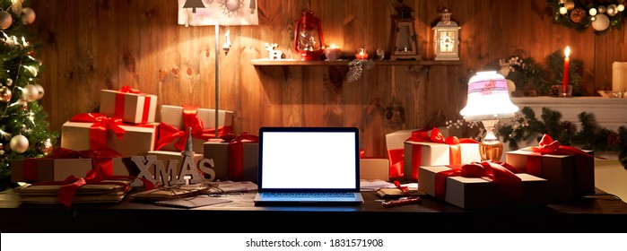 Laptop computer with white blank empty mock up screen on Merry Christmas table with presents gifts, decorated Xmas tree in Santa house background. Ecommerce website online shopping delivery, banner