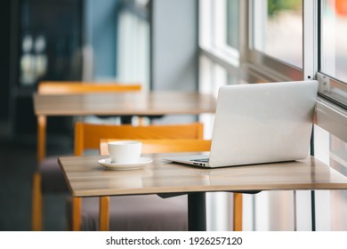 Laptop computer and white coffee cup on wooden table in coffee shop. Relax work time.