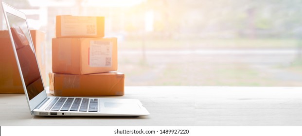 Laptop computer at workplace of start up, small business owner. cardboard parcel box of product for deliver to customer. Online selling, e-commerce, packing concept, Morning light