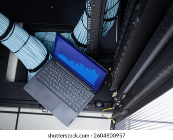 A laptop with a data analysis display sits in a modern server room, surrounded by organized cables, showcasing the intersection of technology and infrastructure.