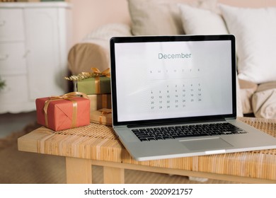 Laptop With December Calendar On Screen Laying On Table In Living Room Decorated For Winter Holidays. Planning Christmas Family Activities. 