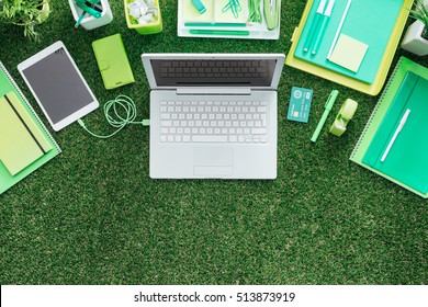 Laptop, digital tablet and office supply on lush grass, green business and technology concept