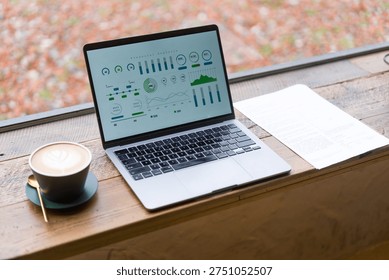 Laptop displaying data analytics charts on a wooden windowsill beside a coffee cup in autumn light