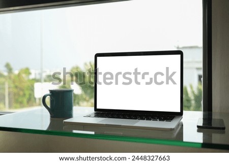 Laptop with empty screen and cup of coffee on table near window. Empty screen for your text message