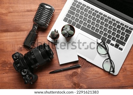 Laptop with eyeglasses, sticky notes, microphone and photo camera on wooden background