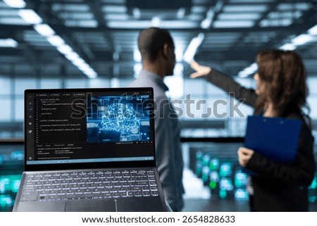 Laptop in front of data center technicians in blurry background deploying AI driven management tools, inspecting server clusters, updating network topologies, validating storage integrity