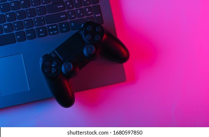 Laptop And Gamepads With Blue Pink Neon Vibrant Light. Gaming, Leisure And Entertainment Concept. Top View