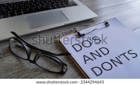 Laptop, glasses and paper clipboard with text DO'S AND DON'TS on table. 