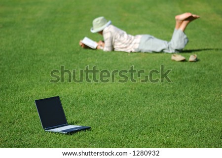 Laptop in Grass and Woman Lays in Grass Reading
