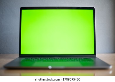 Laptop With Green Screen On Wood Table On Blur Background In Technology Concept.