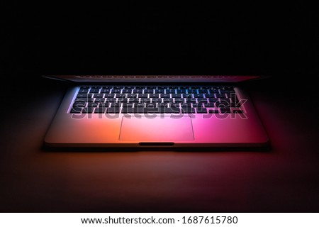 a laptop half closed in the dark with colourful glow