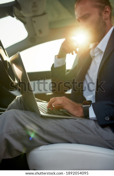 Laptop in\
hands of young working caucasian businessman sitting in luxury car\
in sunlights. Success and lifestyle\
concept