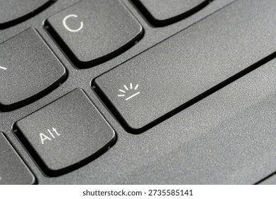 Laptop keyboard backlight toggle key closeup with illumination icon on spacebar, black matte plastic keys, computer shortcut hotkey button, technology control interface, macro detail, selective focus