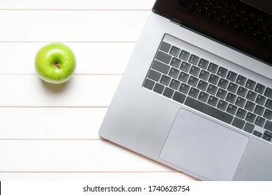 Laptop keyboard and green apple on white wooden table. Top view. Concept distance learning