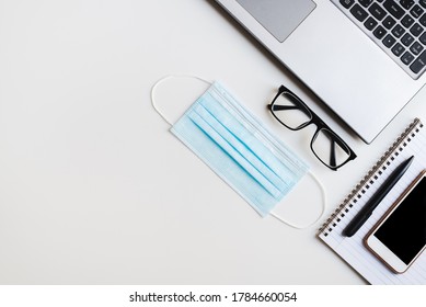 Laptop Keyboard, Medical Face Mask, Reading Glasses, Notebook, Pen And Mobile Phone On White Office Desk. New Normal At Work