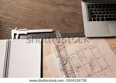 Laptop keypad, rulers and handtool, open copybook surrounded by unfolded blueprints with sketches of new building drawn by engineer