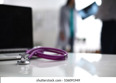 Laptop And Medical Stethoscope On The Desk , Doctors Standing In The Background.