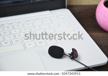 Laptop and microphone on a wooden table flower in the background. Journalist, online training, remote work, online games
